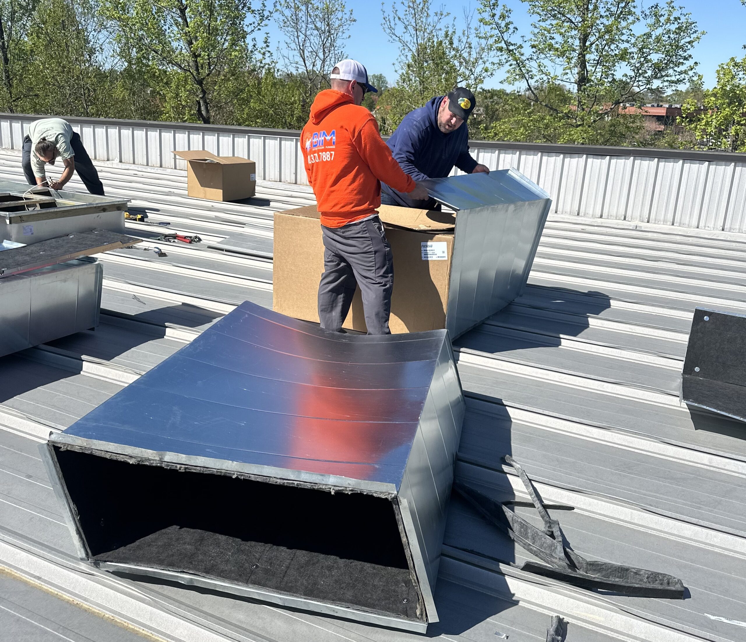 Technician installing ductwork and rooftop HVAC unit at BIM commercial site