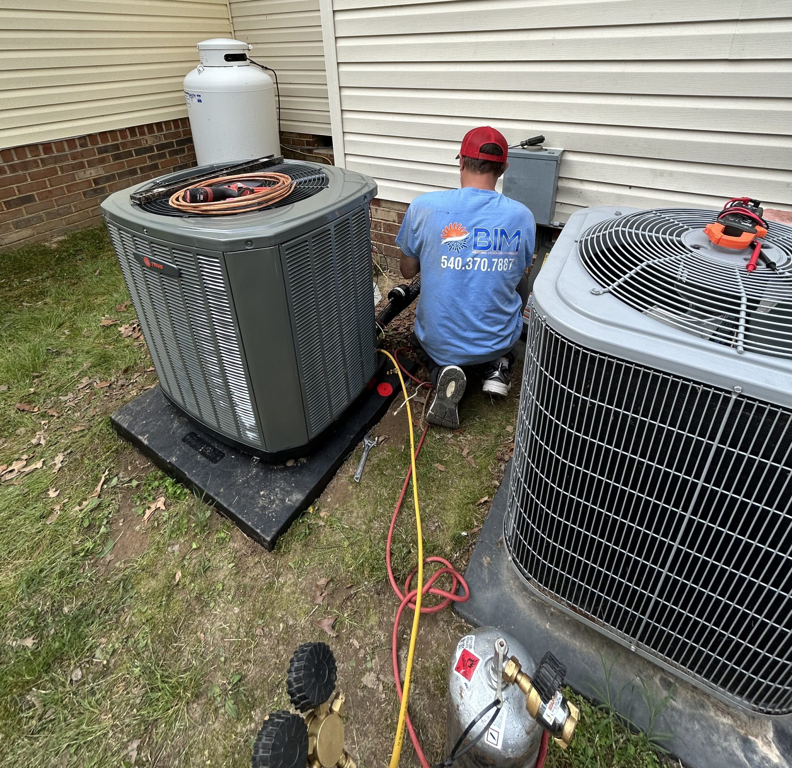 BIM Heating and Cooling technician installing new outdoor AC unit at home patio